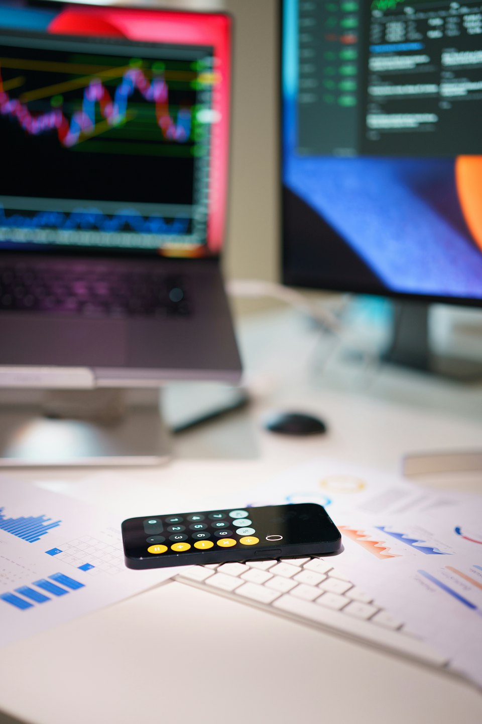 Smartphone pe documente financiare lângă laptop cu grafice bursiere.
